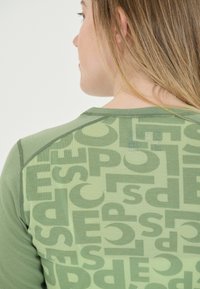 Groene T-shirt met een gestructureerd, gelaagd ontwerp en grote, overlappende letters in verschillende tinten groen op de rug.