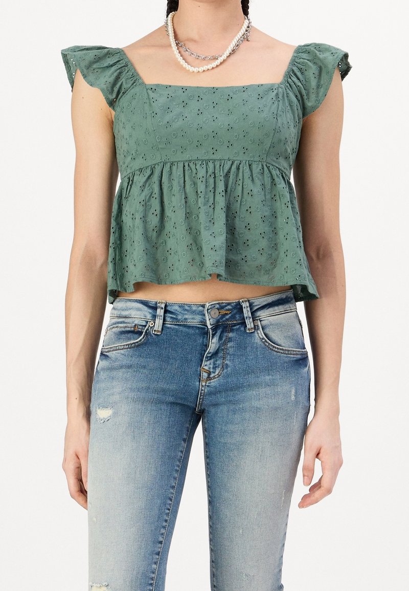 Top corto verde con estampado floral y escote cuadrado, con mangas rizadas, combinado con jeans de mezclilla claros y desgastados.