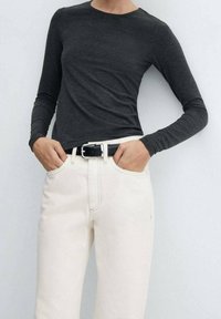 Top de manga larga negro combinado con jeans color crema; cuenta con un cinturón negro con hebilla plateada. Textura suave, ajuste casual.