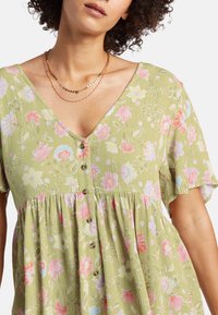 Vestido estampado floral en un suave tono verde, con un escote en V pronunciado, mangas cortas y detalle de botones. Acentuado con flores en tonos rosa y azul.