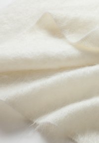 Tessuto bianco morbido con una trama soffice, caratterizzato da delicate pieghe e una leggera lucentezza, che ne mette in risalto la qualità leggera e ariosa.