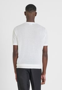 Jersey blanco de manga corta con escote redondo. Textura suave y ligera, con acabados acanalados en contraste en las mangas y el dobladillo.
