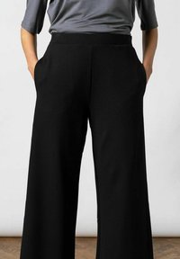 Zwarte wijde broek van soepele stof, met zijzakken en een elastische tailleband. De zoom valt net boven vloerniveau.