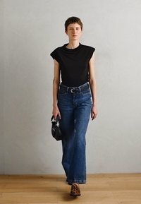 Svart kortermet topp, høyhåndte blå denim flare jeans, svart håndveske og beige leopardmønstret fottøy, satt mot en lys bakgrunn.