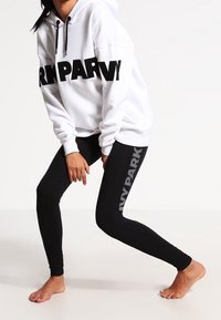 Felpa bianca con testo "IVY PARK" nero, abbinata a leggins neri con "IVY PARK" in grigio. Tessuto morbido e vestibilità comoda.