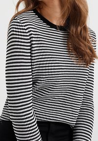 Maglione a motivi bianco e nero con scollo rotondo e maniche lunghe, caratterizzato da un design testurizzato a forma di diamante.