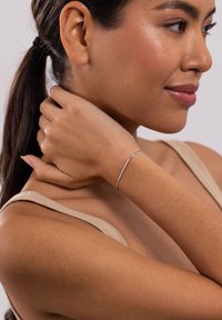 Dünner silberner Armreif am Handgelenk, mit einem glatten, minimalistischen Design. Der Hautton des Modells harmoniert mit dem Armband vor einem neutralen Hintergrund.