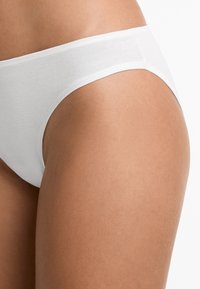 White cotton brief with a smooth texture and a high-cut design, featuring a seamless waistband for comfort and minimal visible lines.