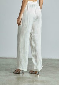Pantalons blancs à jambe large avec une finition texturée et une taille élastique, associés à des sandales à talons argentées avec des accents décoratifs.