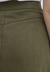 Olivengrønn teksturert skjørt med en glatt, matt overflate. Har subtil søm og en tettsittende midjebånd, som gir et enkelt, elegant design.
