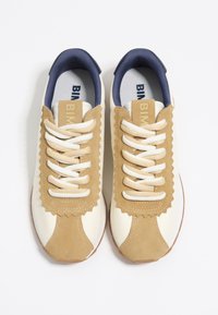 Zapatillas en tonos marrón y crema con cordones blancos, detalles en ante con forma de ola y un cuello forrado en azul marino. Suela de goma para agarre y durabilidad.