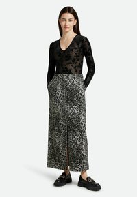 Zwarte doorschijnende bodysuit met lange mouwen en bloemenpatroon, gecombineerd met een maxi rok in panterprint. De rok heeft een split aan de voorkant en zakken.