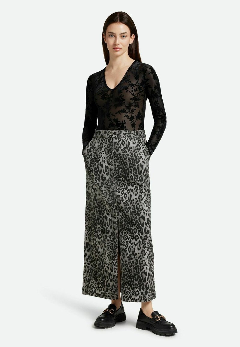Zwarte doorschijnende bodysuit met lange mouwen en bloemenpatroon, gecombineerd met een maxi rok in panterprint. De rok heeft een split aan de voorkant en zakken.