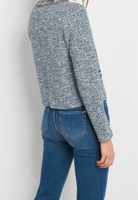 Texturerad blå tweedjacka med en kortad passform, som har långa ärmar och en volangkrage, i kombination med skräddarsydda blå jeans.