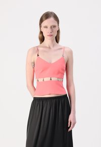 Coral fitted crop top with thin straps, featuring decorative silver hardware at the waist. Smooth fabric, paired with a black flowing skirt.