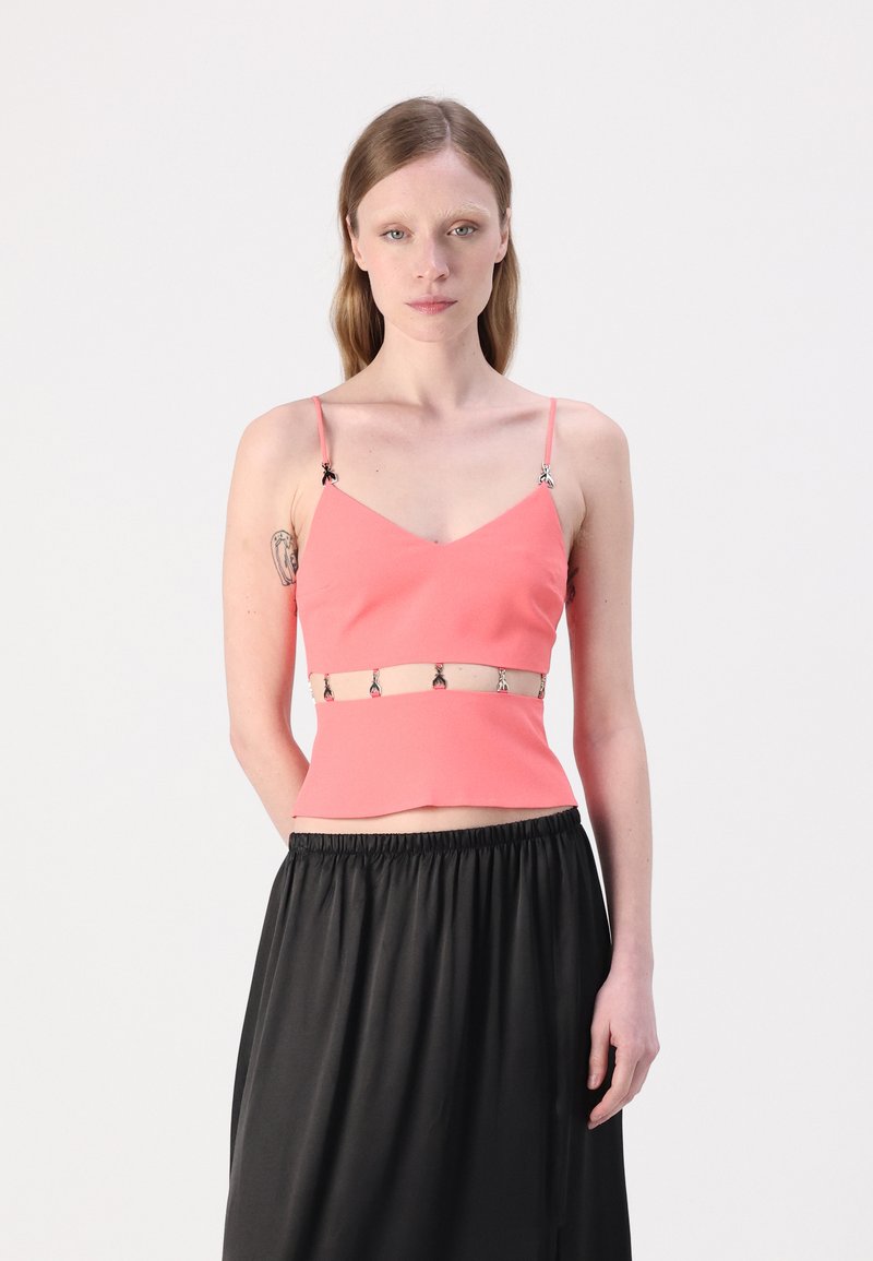 Coral fitted crop top with thin straps, featuring decorative silver hardware at the waist. Smooth fabric, paired with a black flowing skirt.