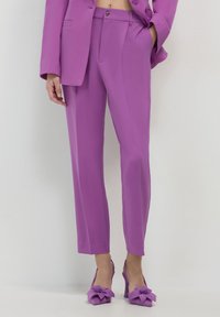 Pantaloni su misura viola e scarpe con tacco abbinate con dettagli a fiocco. Tessuto morbido e vestibilità slim, completati da un blazer su misura.