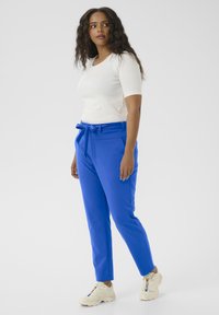 modré kalhoty s páskem na vázání, slim fit, boční kapsy a hladká textura. V kombinaci s bílým topem s krátkým rukávem a světlými teniskami.