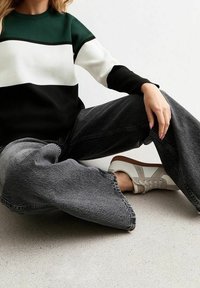 Sweter w czarne, białe i zielone poziome paski; połączony z oversize'owymi, wyblakłymi czarnymi dżinsami; białe sneakersy z szarymi akcentami.