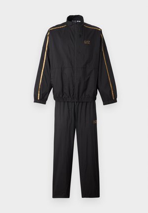Tuta nera con giacca zip-up, polsi regolabili e pantaloni con vita elasticizzata. Accenti dorati lungo le maniche e il logo.