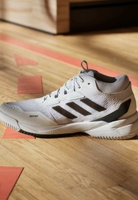 Białe sportowe buty z teksturowaną cholewką, trzema czarnymi paskami, brandingiem ADITUFF oraz solidną, amortyzującą podeszwą.