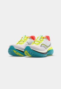Zapatillas de correr con una parte superior de malla blanca, cordones de neón amarillo, acentos rojos y una suela color teal con detalles amarillos. Diseño elegante adecuado para atletas.