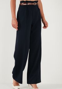 Pantaloni evazați de culoare bleumarin, confecționați dintr-un material neted, având un curea texturată cu embossing de crocodil, de culoare marron, cu o cataramă argintie.