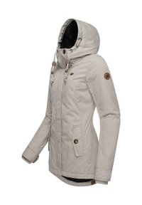 Light beige waterproof jacket with a hood, featuring side pockets, drawstrings, and a soft black lining. Brown logo patch on sleeve.