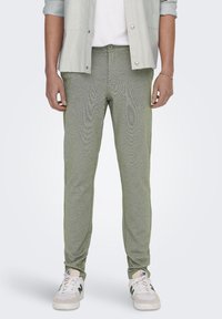 Pantalones deportivos verdes texturizados con un corte ajustado, que cuentan con una cintura con cordón y un detalle sutil a lo largo de las costuras, combinados con zapatillas blancas.