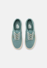 Ljus teal canvas sneakers med rund tå, vit gummisula, beige snören och en etikett på sidan med Vans-logotypen.