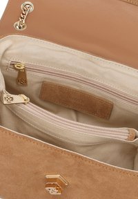 Inderside af beige ruskindspung med to lynlåskompartimenter, guldfarvet hardware og et lysebrunt stoffor med et mærkebånd.