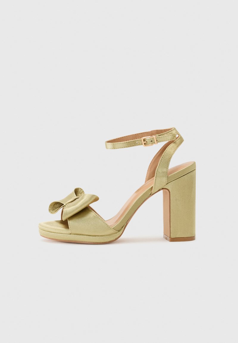 Sandal de salto alto em cetim verde com um laço detalhe na tira da frente, tira ajustável no tornozelo e um salto quadrado grosso.