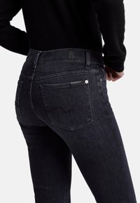 Jeans en denim foncé avec une coupe ajustée, dotés d'une taille haute, de poches arrière, d'un détail de couture subtil et d'une étiquette en cuir de marque à la taille.