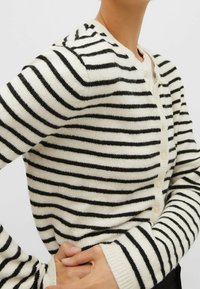 Striped cardigan in cream and black, featuring a button closure, ribbed cuffs, soft texture, and a fitted silhouette.