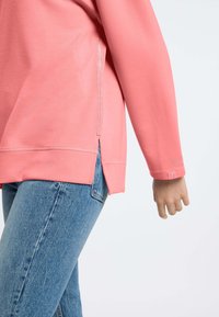 Koraalkleurige trui met een relaxte pasvorm, zijsplitten en ribgebreide boorden; gemaakt van een zachte, gestructureerde stof met een subtiele, glanzende accentdetail.