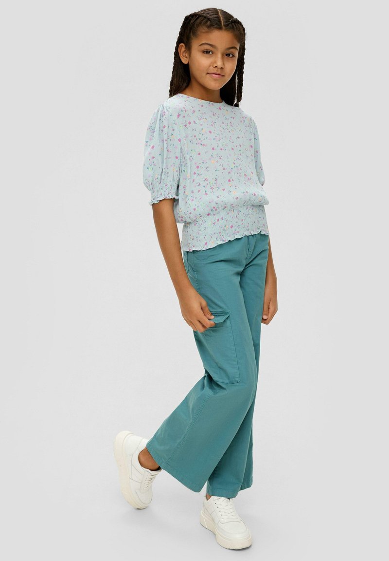 Lichtblauw, bloemenpatroon top met korte pofmouwen, gecombineerd met teal wijde cargobroek en witte sneakers.