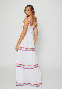 Abito maxi bianco con un corpetto aderente arricciato, spalline a volant rosa e motivi zigzag colorati in arancione, rosa e blu sull'orlo.