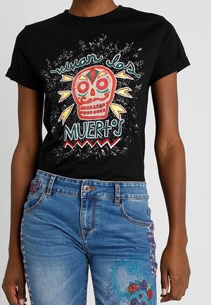 Zwart T-shirt met kleurrijke Dia de los Muertos-schedel en de tekst "Vivan los muertos", gedragen met blauwe jeans met bloemrijke borduursels.