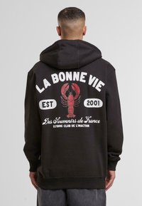 Black hoodie featuring a red lobster graphic, white text saying "LA BONNE VIE EST 2001," and "Des Souvenirs de France" on the back.