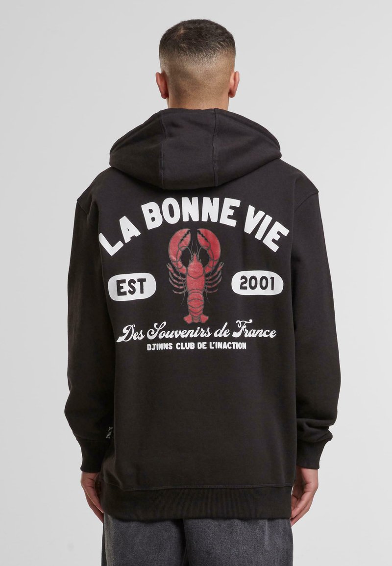 Fekete kapucnis pulóver, piros homár grafikával, fehér szöveggel: "LA BONNE VIE EST 2001", valamint "Des Souvenirs de France" felirattal a hátán.
