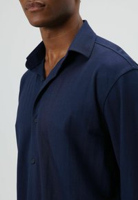 Marineblauw overhemd met knopen, voorzien van een zachte textuur, klassieke kraag en korte mouwen, met twee zichtbare knopen op de knoopsluiting.