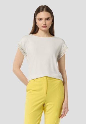 White top with lace trim on short sleeves, paired with yellow trousers. Material appears smooth; round neckline and relaxed fit.