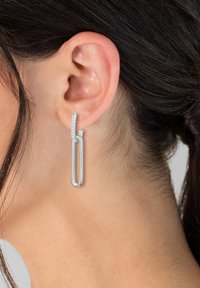 Sudraba pilienu auskari ar elegantu, izstieptu cilpas dizainu un maigu spīdumu augšpusē. Gluda apdare, minimālisma stils.