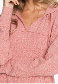 Sudadera rosa con capucha y diseño de escote en V, textura suave y detalle de cordón. Cuenta con mangas largas y un ajuste relajado.