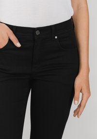 Zwarte denim jeans met een aansluitend ontwerp, vijf zakken en een metalen knoopsluiting. Gladde textuur met subtiele stikdetails.