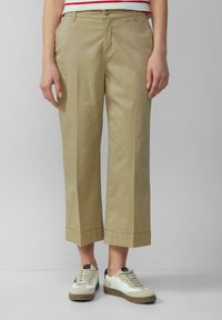 I pantaloni beige a gamba larga presentano un tessuto in cotone liscio, una chiusura a un pulsante e un orlo accorciato. Abbinati a sneakers bianche e beige.