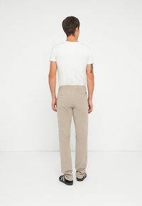 Pantalons en velours côtelé beige avec une coupe droite, deux poches arrière et des détails de couture subtils. Associé à un t-shirt blanc ajusté.