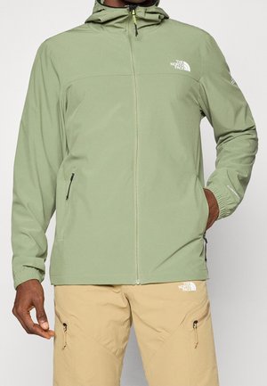 Mann trägt hellgrüne North Face Kapuzenjacke mit Reißverschlusstaschen und beige North Face Hose mit Reißverschluss-Oberschenkeltaschen.