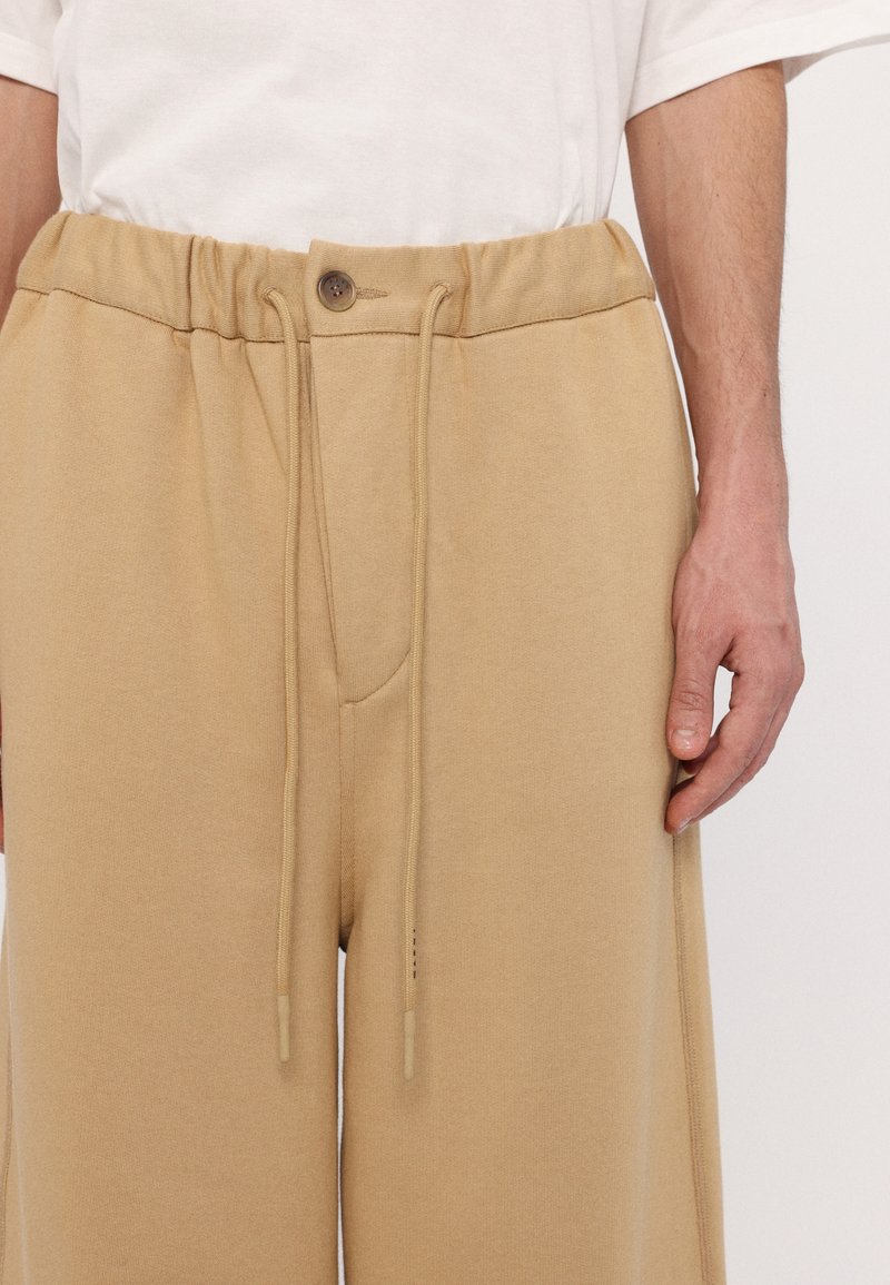 Beige Jogginghosen mit elastischem Bund, Kordelzug und einem Knopf. Mit einer Seitentasche und weichem, strukturiertem Stoff.