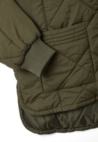 Giacca in olive green trapuntata con polsini a coste, motivo di cucitura diagonale e tasca laterale integrata nel design.